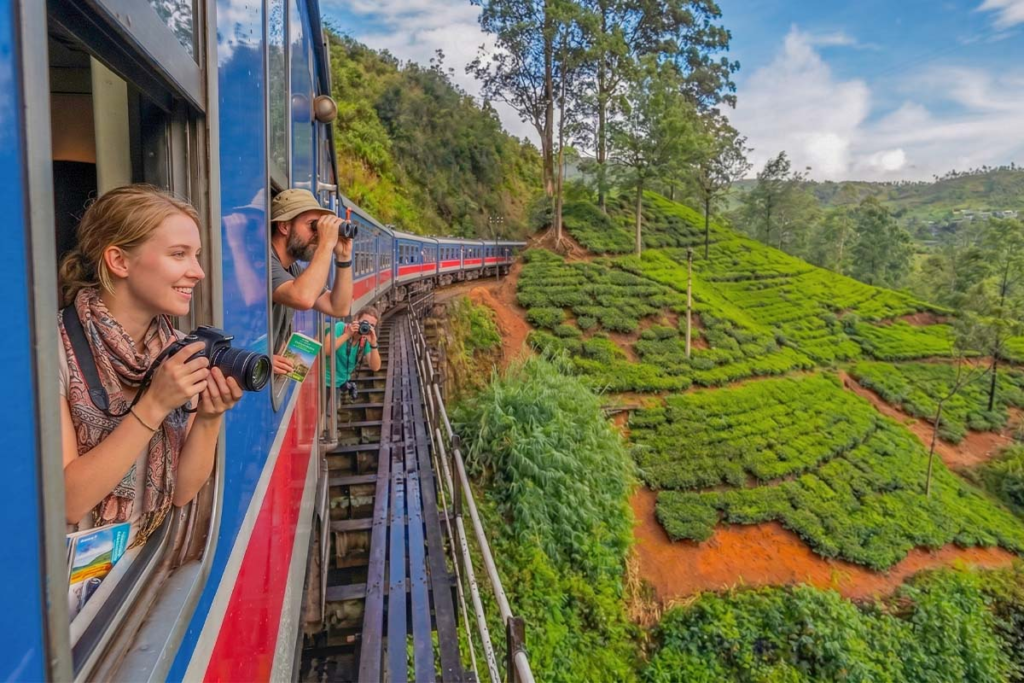 Blue train crossing a scenic bridge surrounded by lush greenery on the Kandy to Ella railway journey in Sri Lanka.