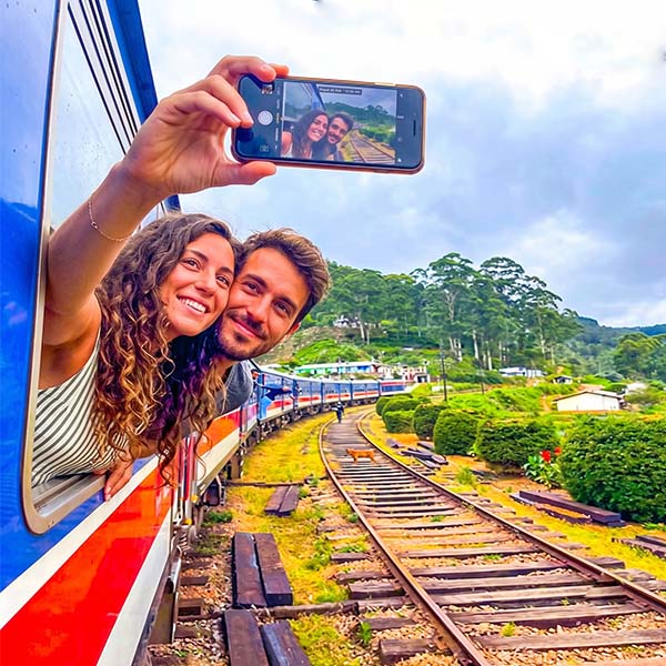 Couple taking a selfie from the famous red train on the scenic Kandy to Ella railway route through Sri Lanka's tea plantations.