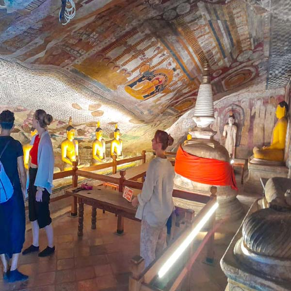 A tourist standing inside the Dambulla Cave Temple admiring a large, golden reclining Buddha statue.