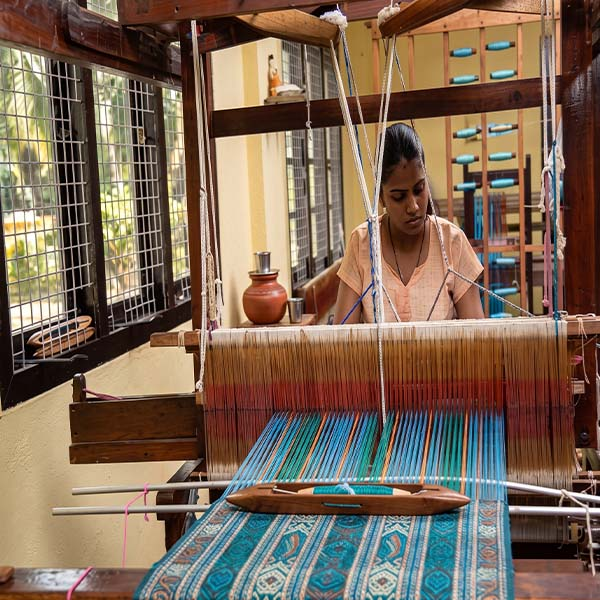 A local village woman operating a traditional wooden handloom to weave colorful fabric.