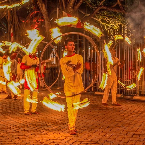 Acrobatic fire dancers performing during the Kandy procession, manipulating large, spinning structures of fire to create dynamic light trails against the night sky.