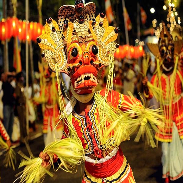 Traditional Sri Lankan performer wearing a vibrant red and yellow Raksha mask dancing at the Kandy Esala Perahera