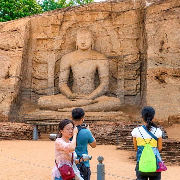 Large seated Buddha statue carved into a solid granite rock face at the ancient Gal Vihara in Polonnaruwa, with visitors observing in the foreground
