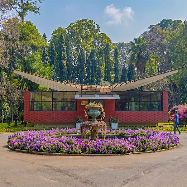 Exterior view of the Royal Orchid House at the Royal Botanical Gardens Peradeniya featuring a modern open-air pavilion, landscaped flower beds, and lush surrounding trees.