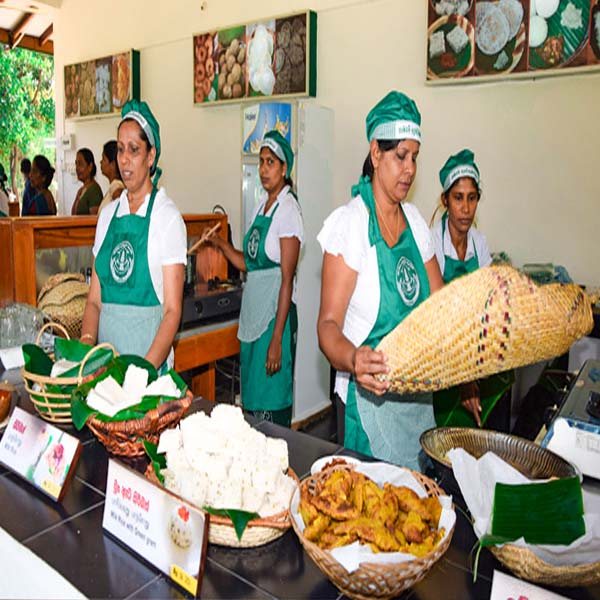 A group of local Sri Lankan women in green aprons and caps serving traditional sweetmeats and savory snacks at the Hela Bojun food outlet.
