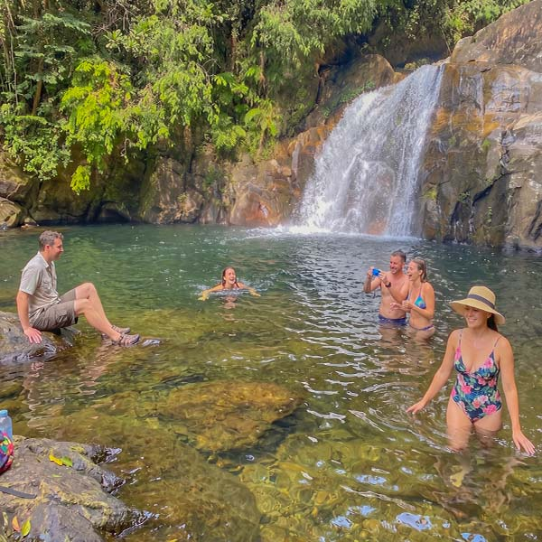 Tourists swimming and relaxing in a natural rock pool at the base of a cascading waterfall in the Sinharaja Rain Forest.