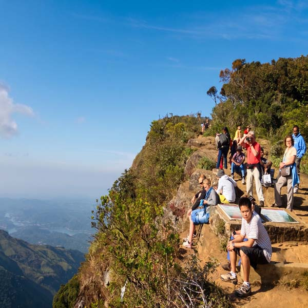 A group of hikers resting near a high precipice, enjoying the sweeping, panoramic views of the steep valley and distant mountains.