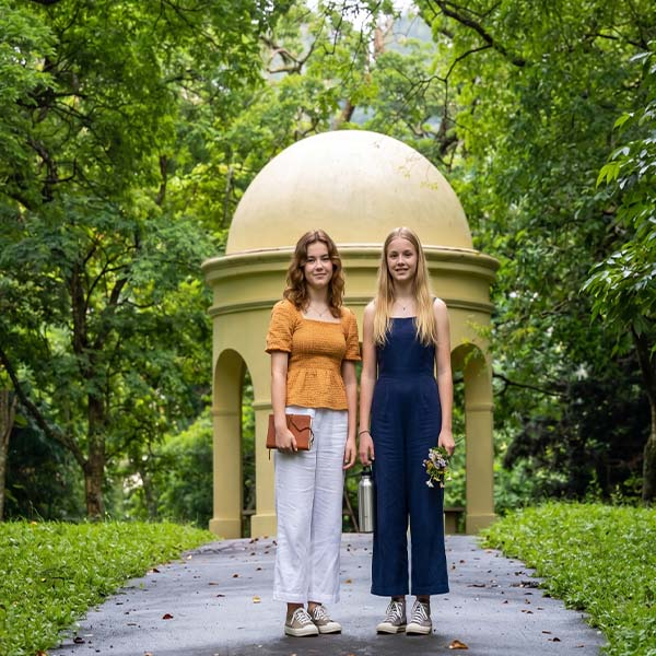 Two visitors standing in front of a white domed pavilion along a paved pathway at the Royal Botanical Gardens Peradeniya.