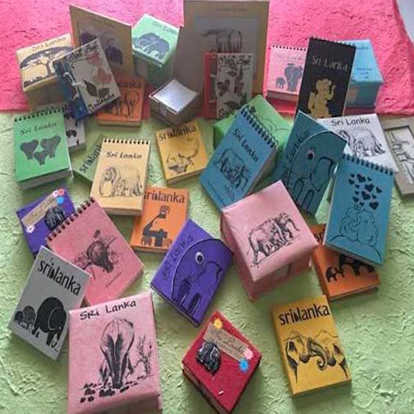 A collection of colorful, handmade eco-friendly notebooks and souvenirs crafted from recycled elephant dung paper, featuring elephant illustrations and "Sri Lanka" text.