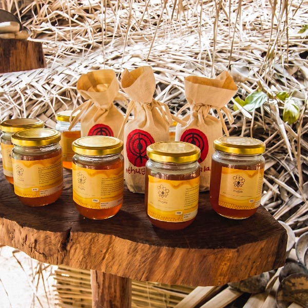 Jars of pure bee honey and packaged handmade crafts displayed on a rustic wooden slab in Rathugala village, Sri Lanka.