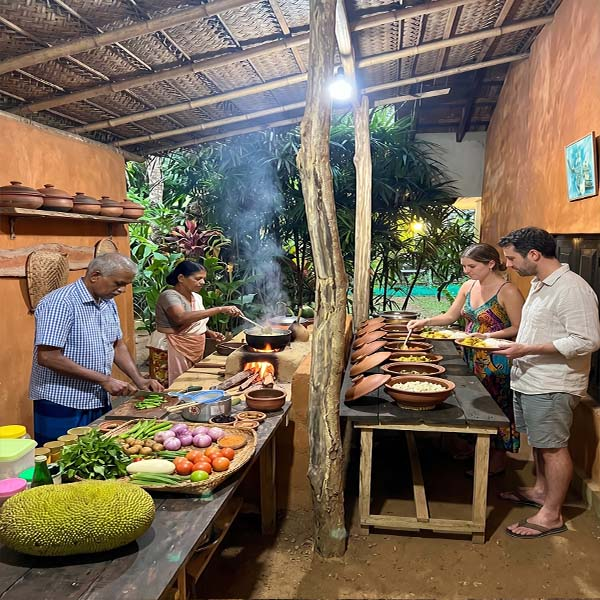 Travelers experiencing an Udawalawe village tour, serving themselves a traditional culinary tasting from clay pots while local villagers cook fresh ingredients over an open hearth.