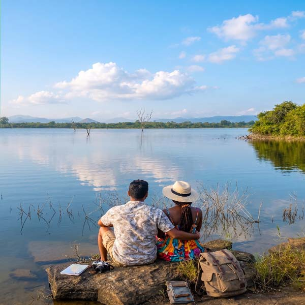 A traveler couple relaxing by the tranquil waters of a scenic Sri Lankan reservoir, enjoying the blue water and distant green shores.