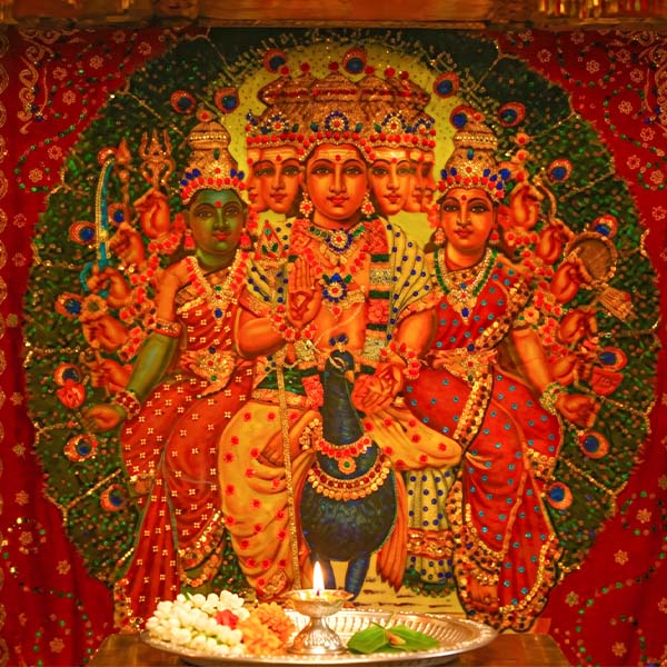A vibrant traditional depiction of the Hindu deity Lord Kataragama (Murugan) with multiple heads and arms, seated on a sacred peacock.