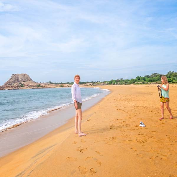 Tourists taking a break on the scenic sandy beach at Yala National Park, with the ocean and rocky outcrops in the background.