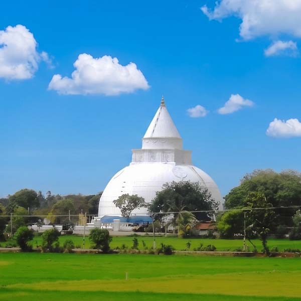 The magnificent ancient white stupa of Tissamaharama Raja Maha Vihara surrounded by lush green landscapes under a bright blue sky.