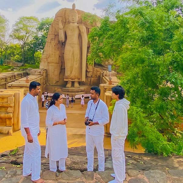 Four people dressed in traditional white temple attire standing on a stone pathway near the Awukana Buddha statue in Sri Lanka.
