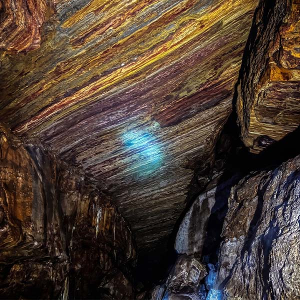 Narrow underground rock cavern passage with mineral-stained walls during the Nil Diya Pokuna trek