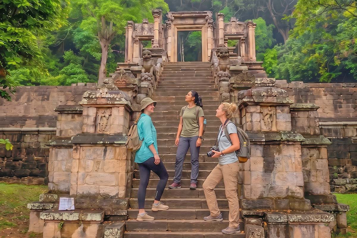 Three tourists exploring the historic stone architecture and ornamental staircase at the Yapahuwa Rock Fortress in Sri Lanka.