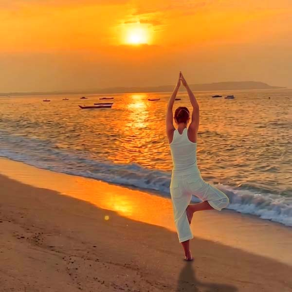Traveler practicing a Tree pose (Vrksasana) on a sandy beach at sunset overlooking the ocean in Sri Lanka.
