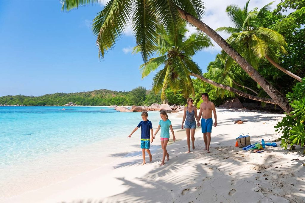 A family walking together on the white sand beach of Unawatuna under tropical palm trees with turquoise ocean water in the background.