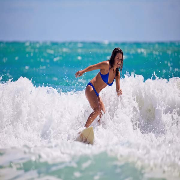 Woman surfing in the rolling ocean waves at Weligama Bay in Sri Lanka with a soft sandy shore in the background.