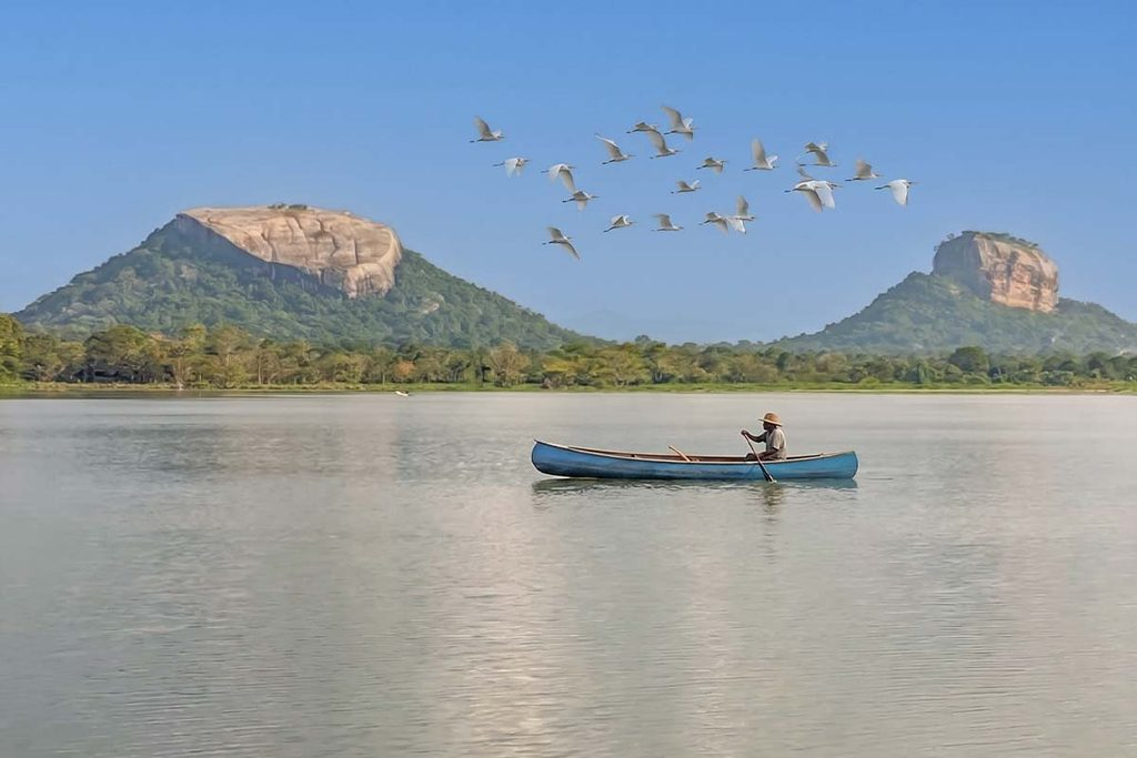 Scenic view of Sigiriya Rock Fortress and Pidurangala  across the tranquil water with a traditional canoe on the lake in Sri Lanka