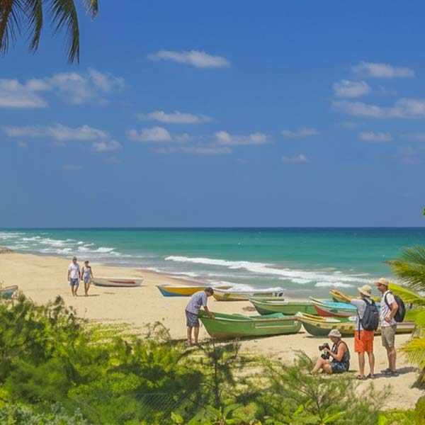 Travelers walking along Nilaveli Beach past colorful fishing boats preparing for a Pigeon Island tour.